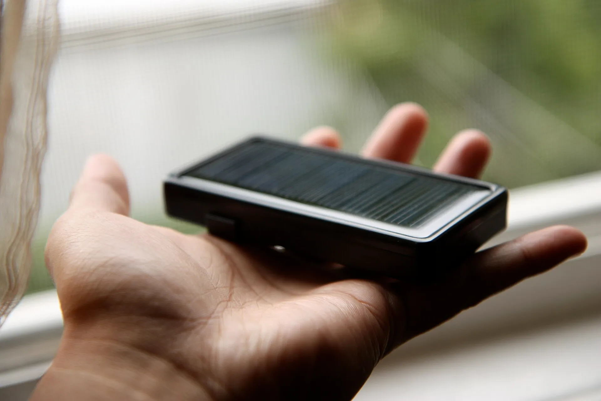 Petite batterie externe solaire tenue dans la paume de la main, près d'une fenêtre