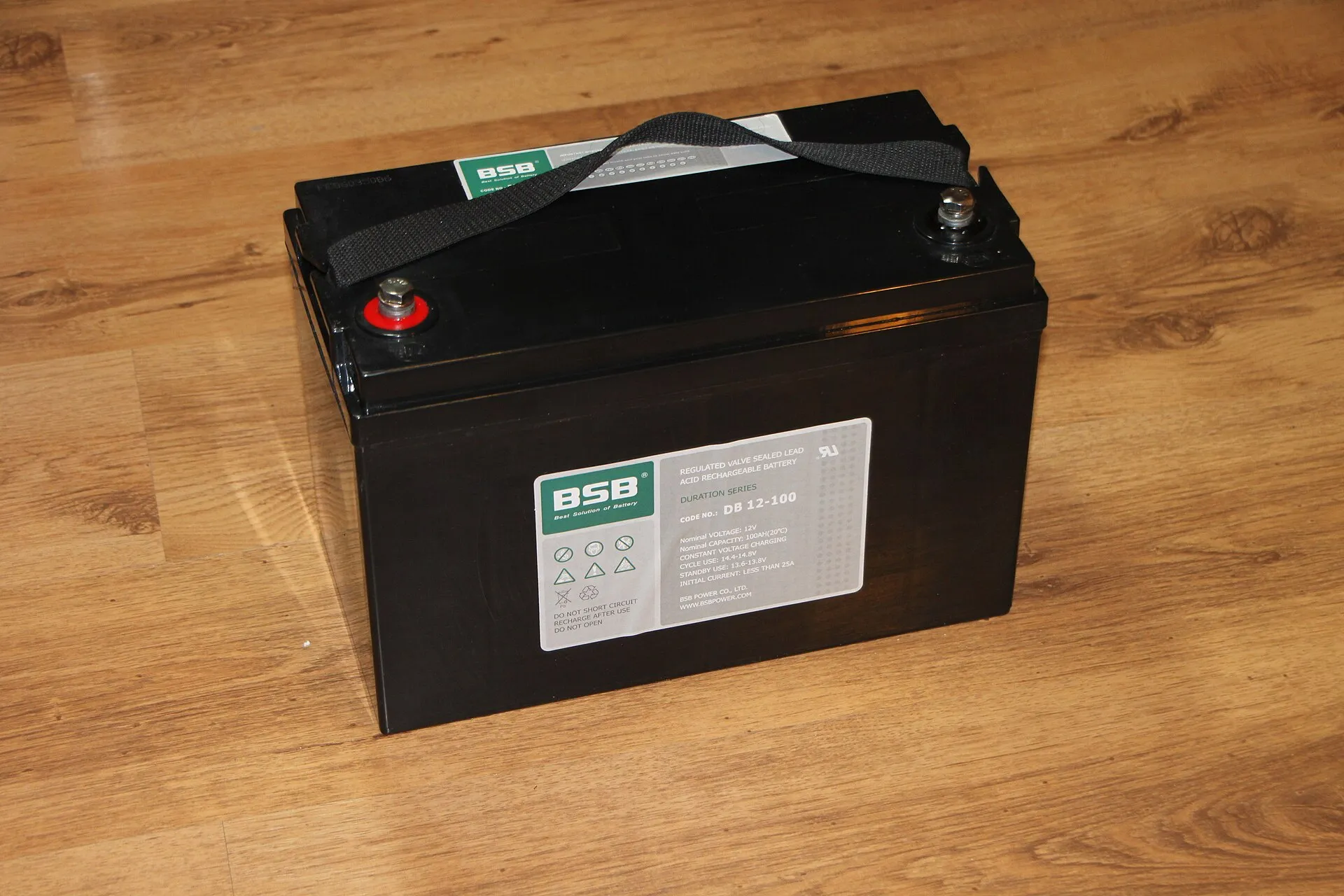 Batterie au plomb étanche de 12 V et 100 Ah, boîtier noir avec poignée, posée sur un parquet