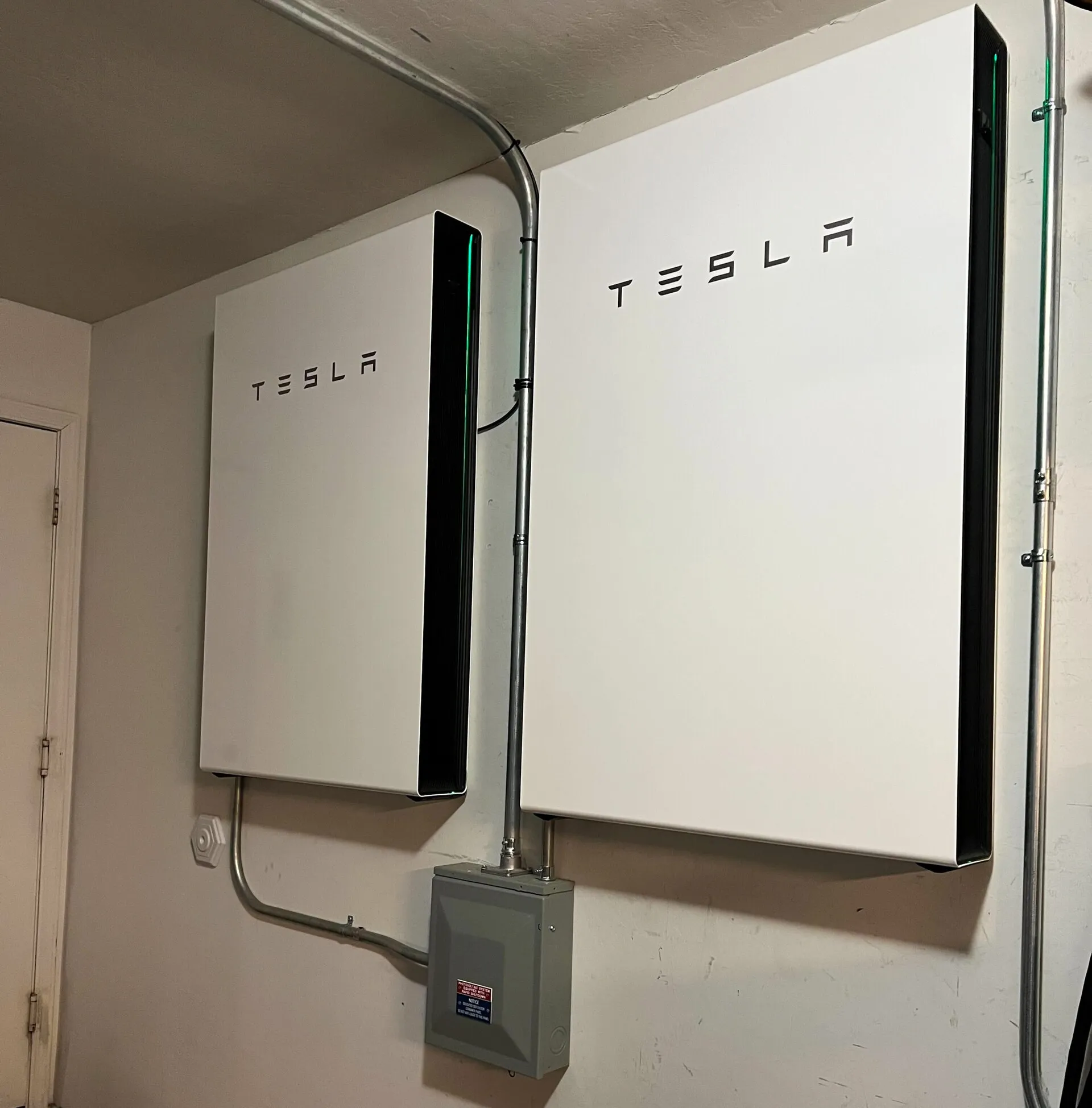 Deux batteries de stockage domestiques fixées au mur d'un local technique, reliées à un boîtier de coupure