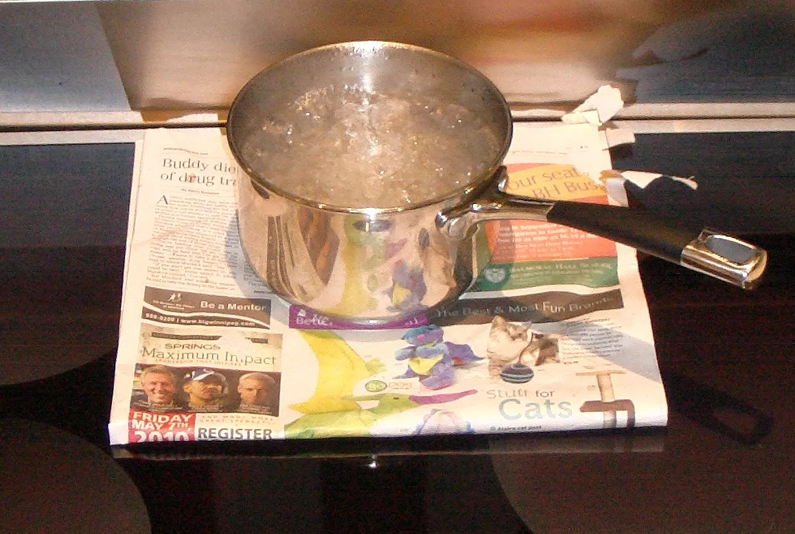Casserole d'eau en ébullition posée sur une feuille de journal, sur une plaque à induction
