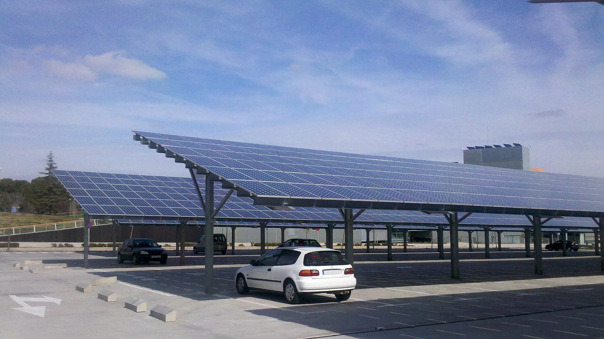 Ombrières photovoltaïques sur un parking universitaire : grands toits de panneaux solaires inclinés sur poteaux, voitures garées dessous