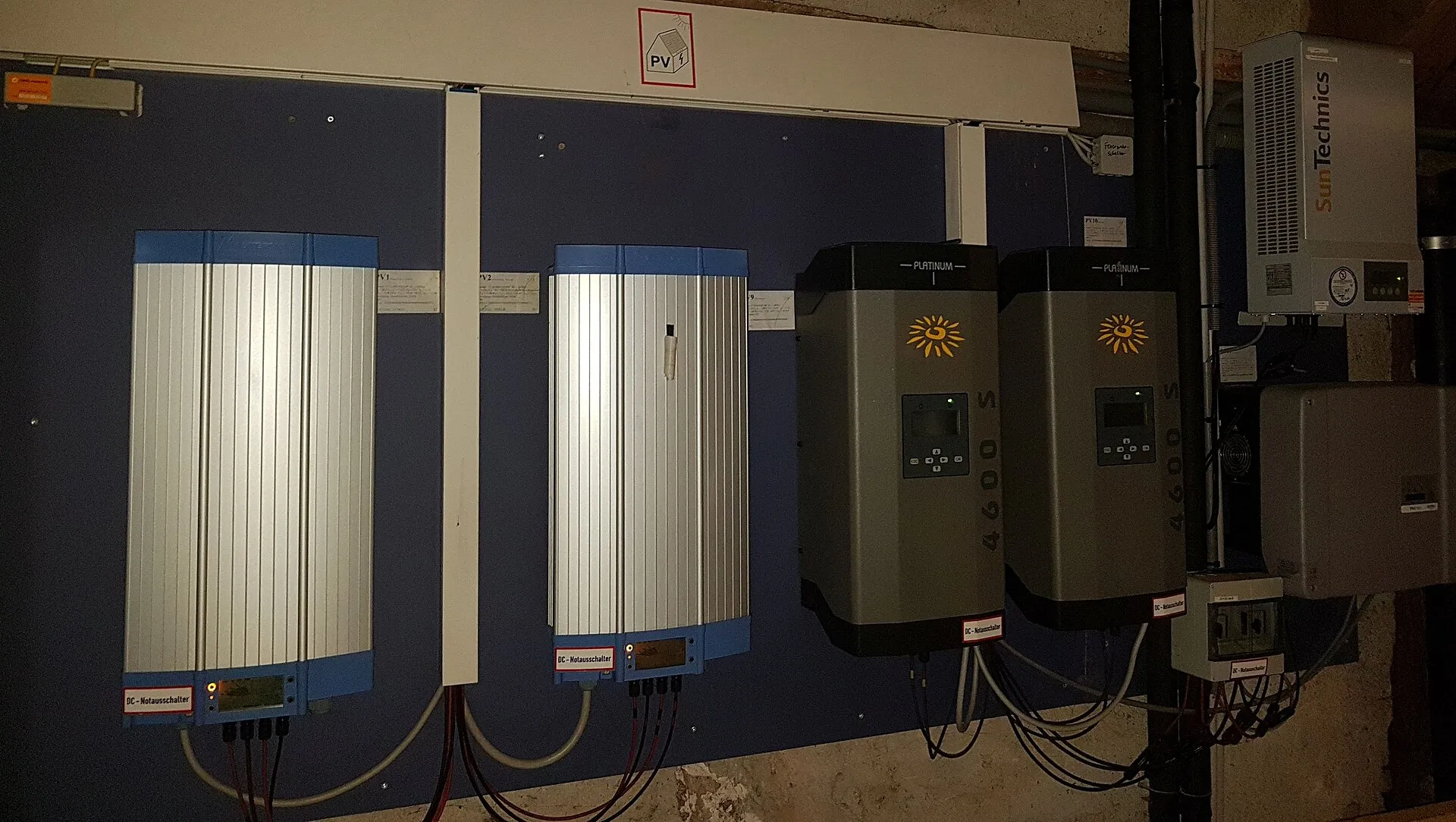 Plusieurs onduleurs photovoltaïques fixés au mur d'un local technique, reliés par des câbles