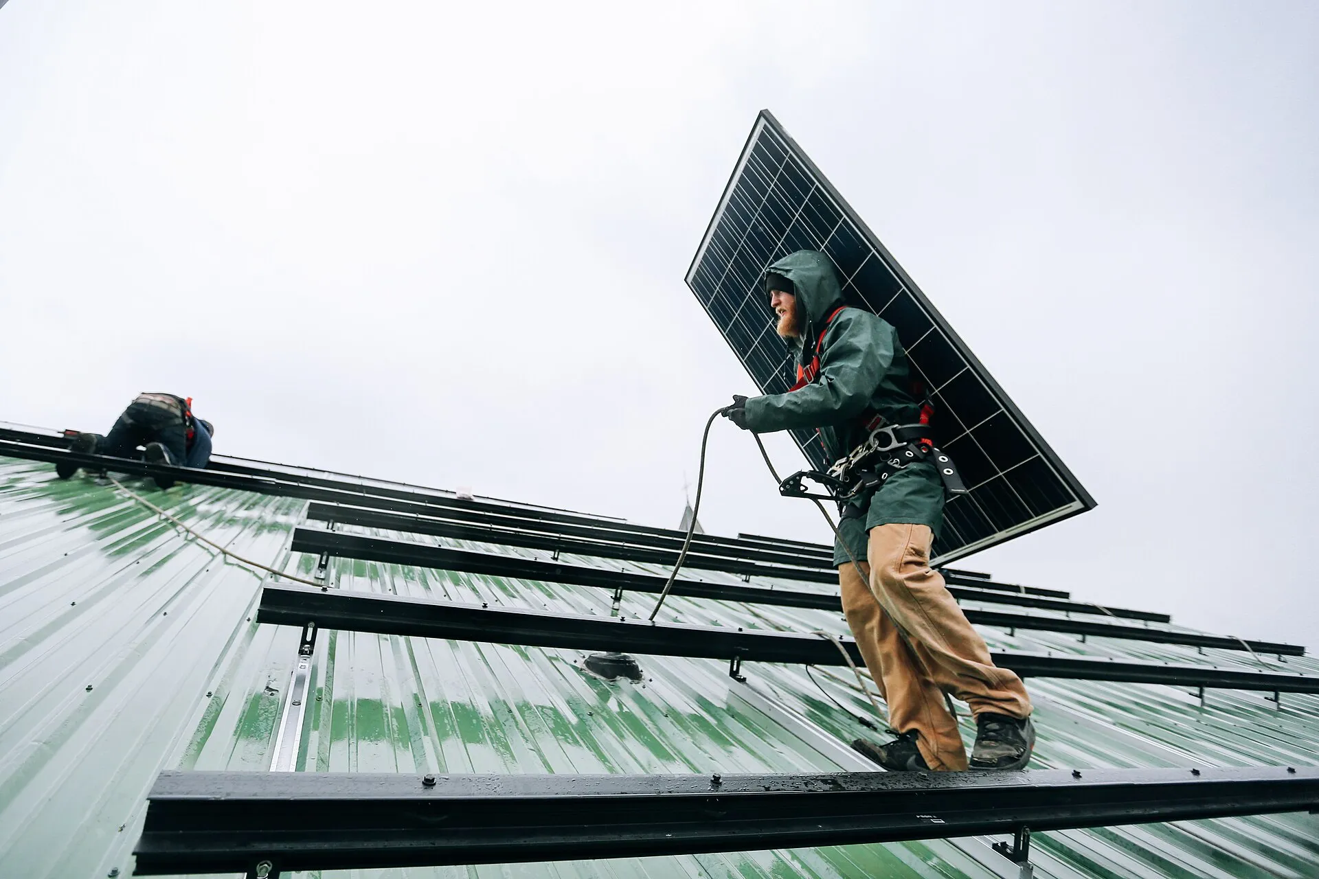 Installateur qui porte un panneau solaire sur un toit en tôle pendant une pose