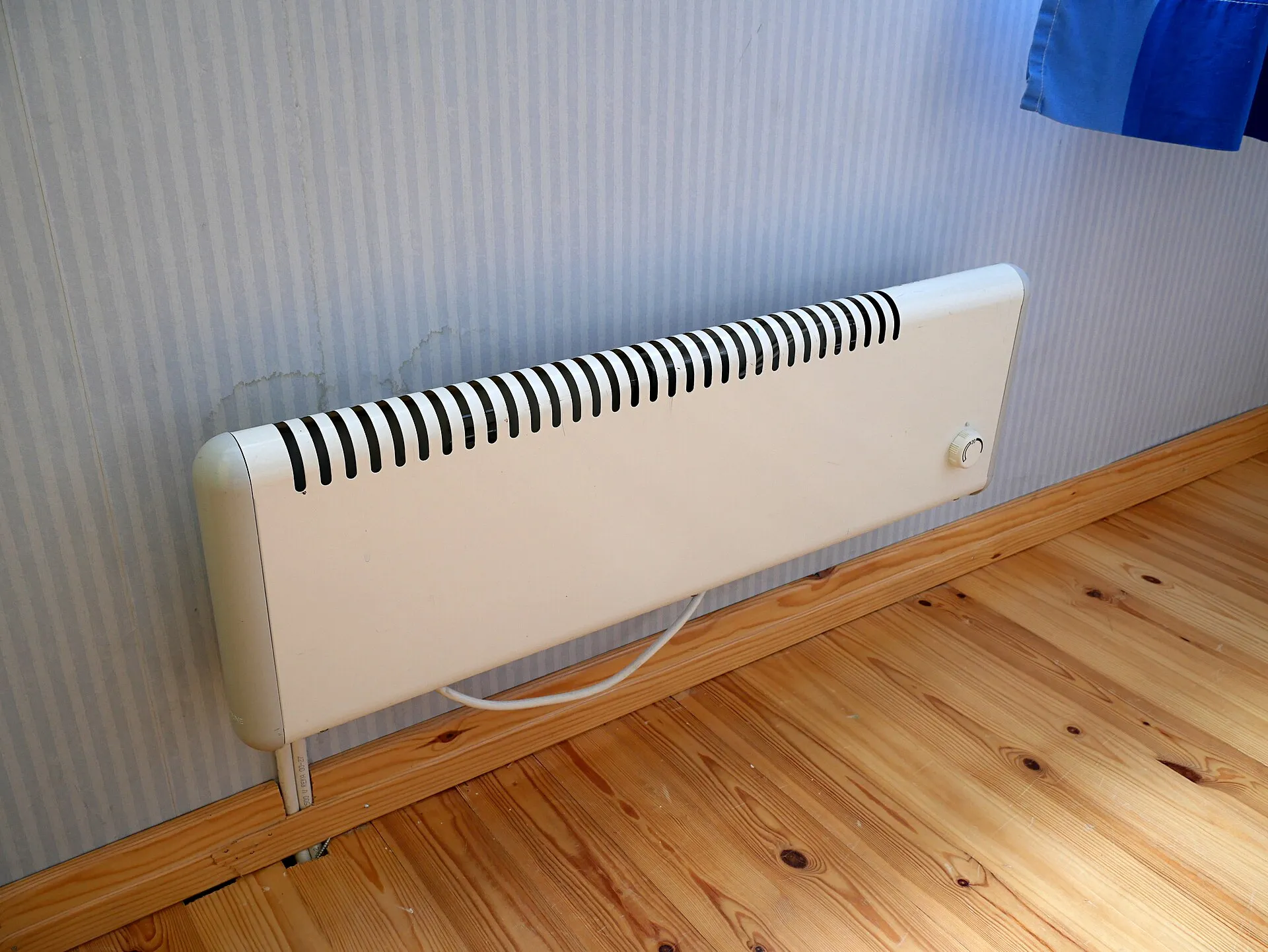 Radiateur électrique blanc fixé au mur, au-dessus d’un parquet