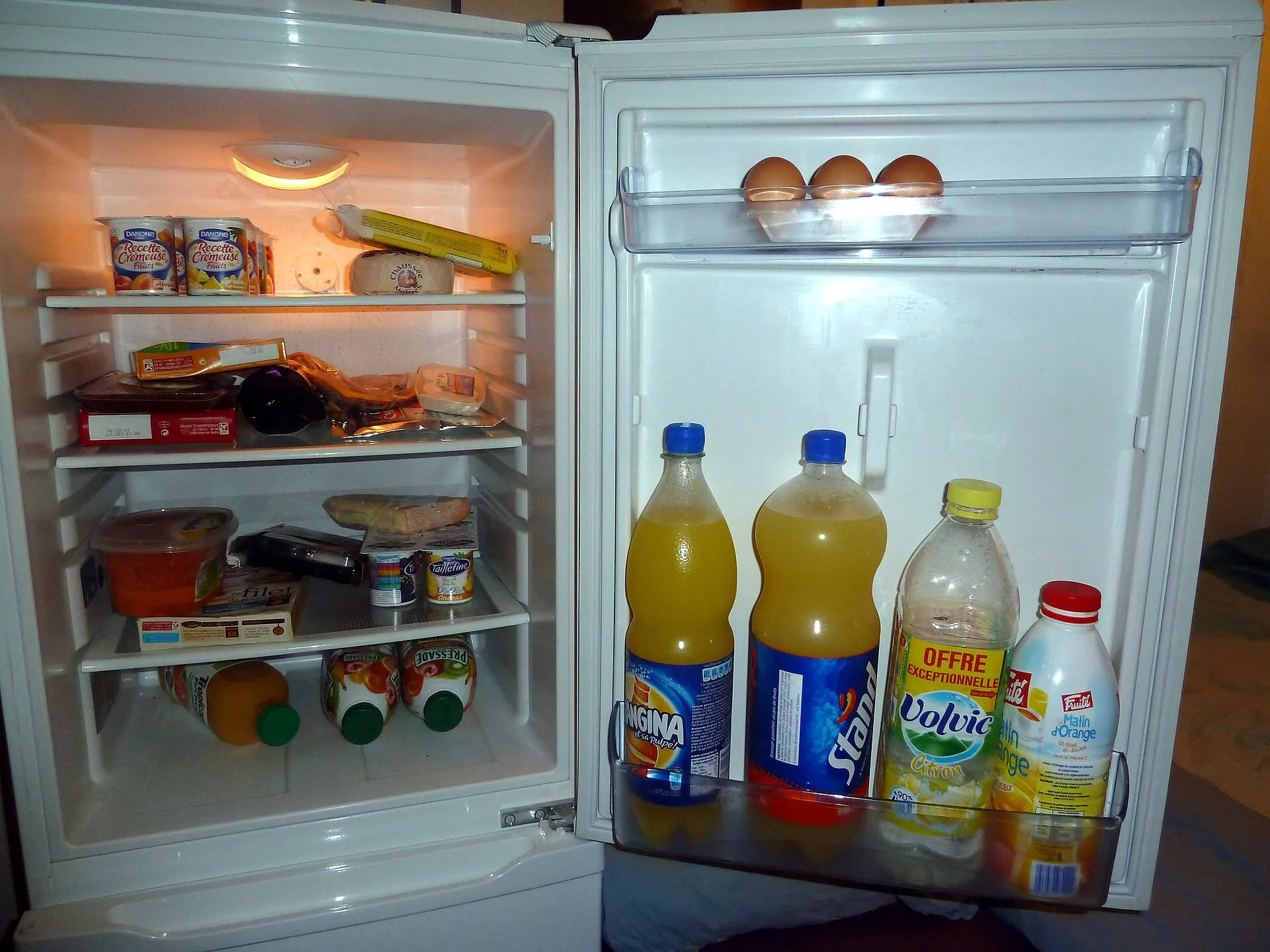 Réfrigérateur ouvert, avec des aliments sur les clayettes et des bouteilles dans la porte